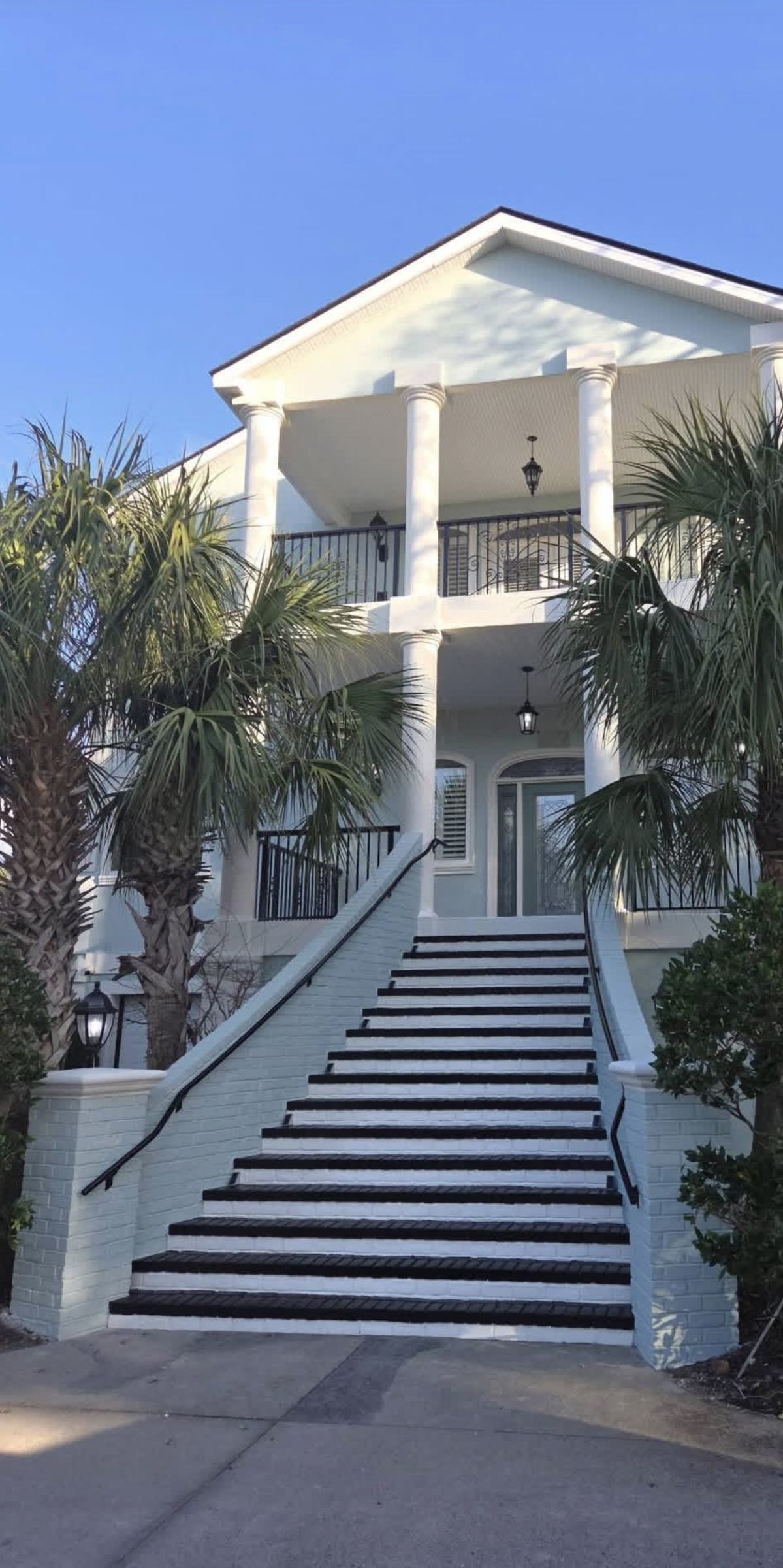 Freshly painted brick staircase leading to a white two-story coastal home with columns and palm trees
